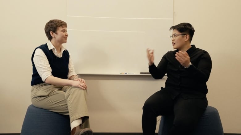 Two people sitting on stools across from each other.