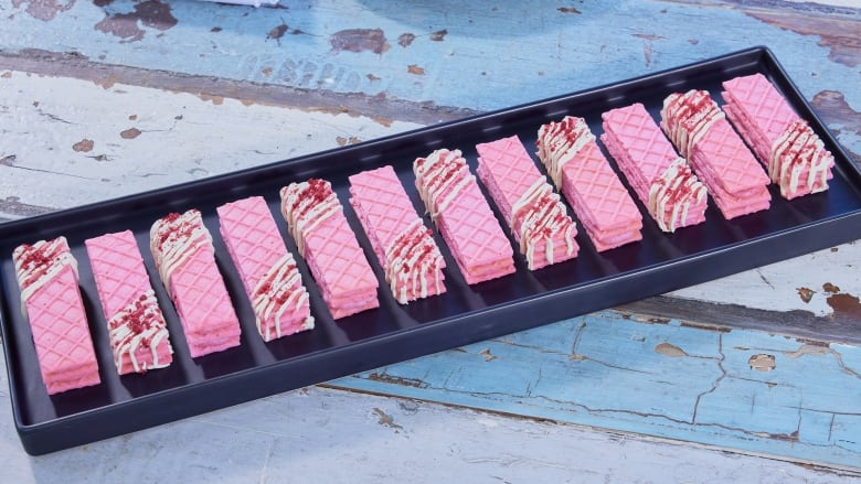 A single row of rectangular, pink, layered wafer cookies with white chocolate drizzle on a black serving platter.