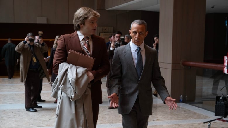 Two men wearing suits walk through a lobby.