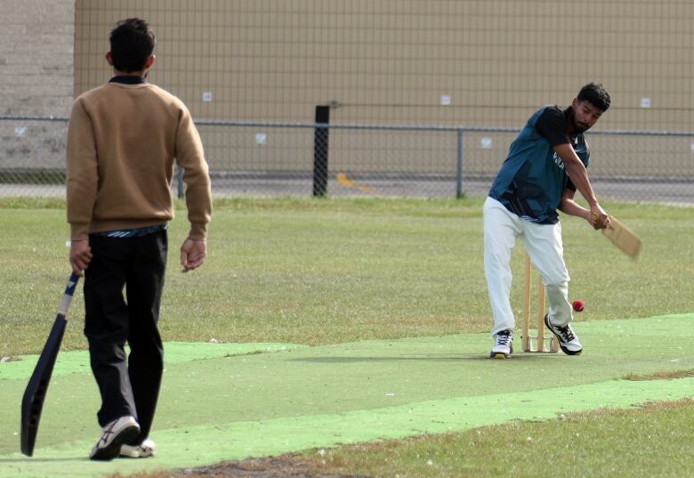 A person holding a cricket bat faces another batter who is about to hit a ball in a pitch.