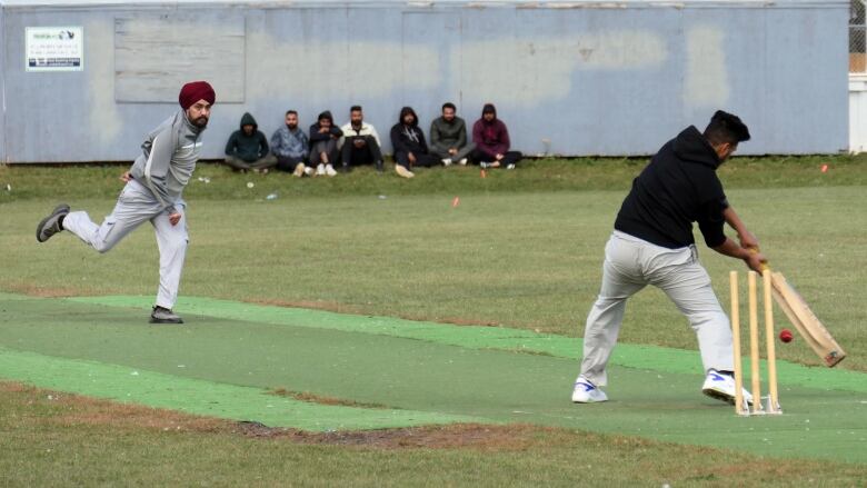 A cricket bowler looks a batter who is about to hit the ball.