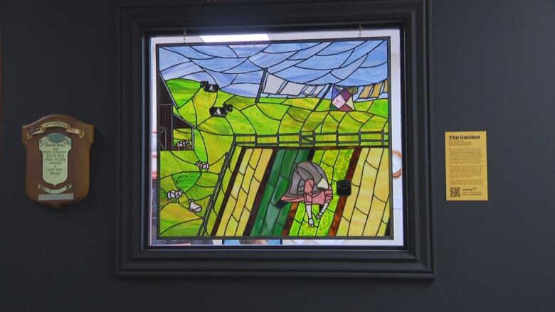 Stained glass artwork depicting woman tending to garden and surrounded by field of livestock.