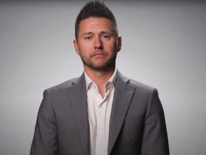 A man wears a white shirt and grey suit.