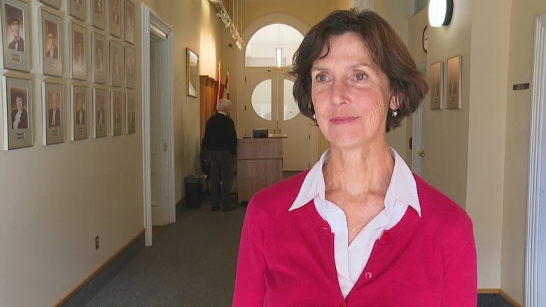 Woman with red sweater over white blouse standing in hallway.