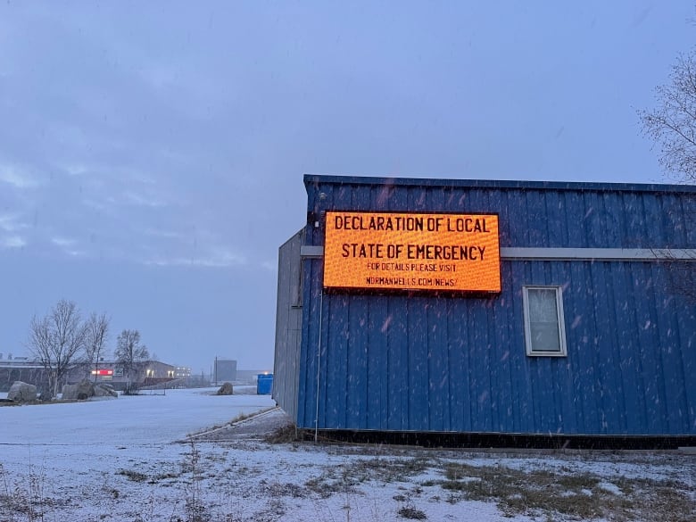 A bright orange sign declares a local state of emergency on the side of a blue building, while snow falls.