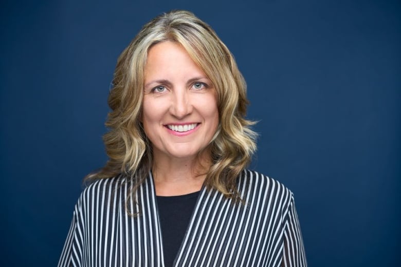 A woman with dark blond hair and a striped blazer smiles at the camera. 