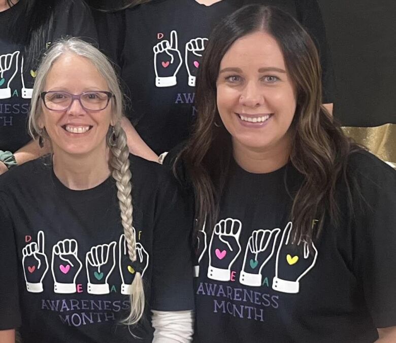 Two women wearing similar shirts. The shirt has illustrations of sign language and it says at the bottom 