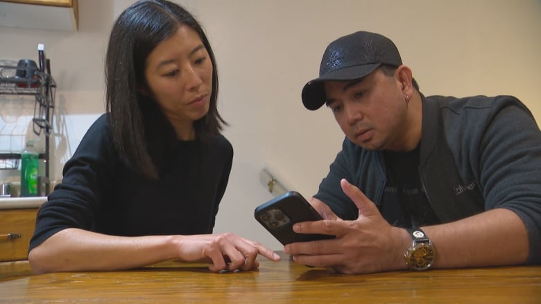 A man and a woman look at a cell phone in the man's hand.