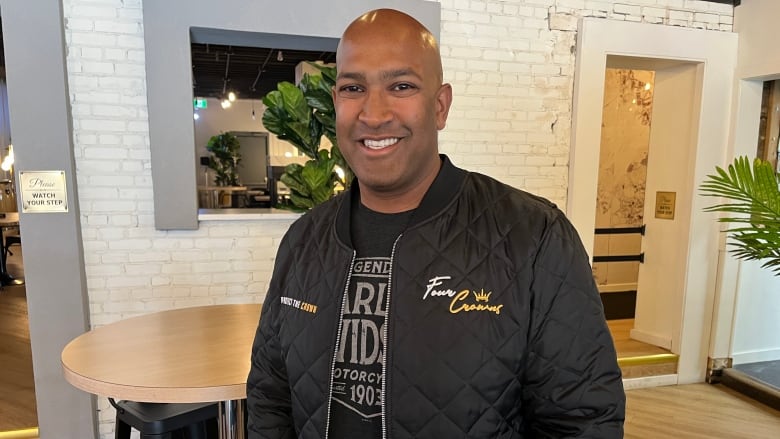 A man in a black bomber jacket smiles to the camera.