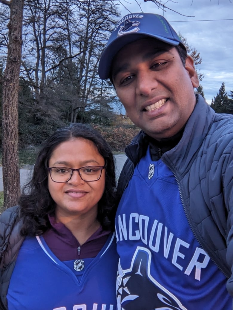 Two South Asian people smile while wearing Vancouver Canucks jerseys.