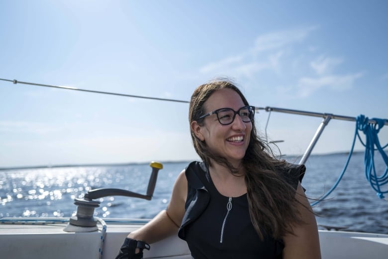 A woman smiles and looks off camera while sitting on a sailboat.