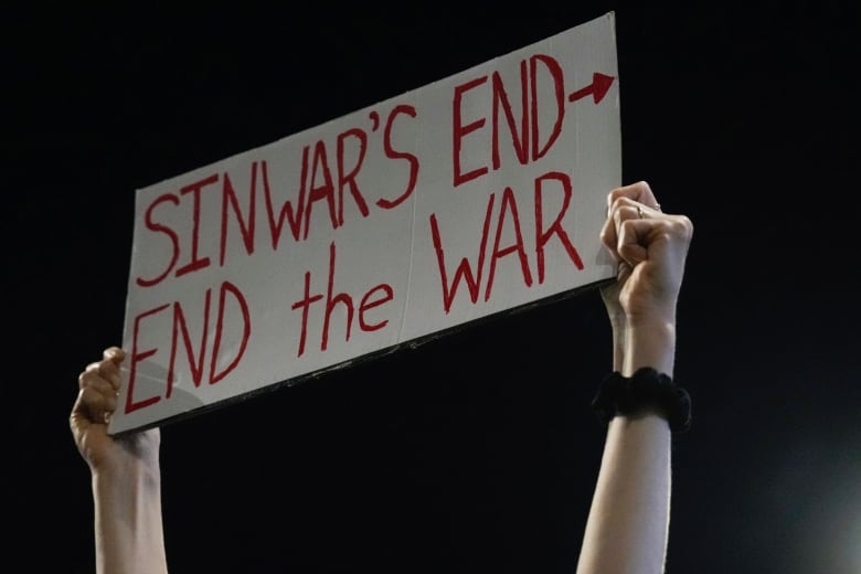 A pair of hands hold a sign that says Sinwar's end, end the war.