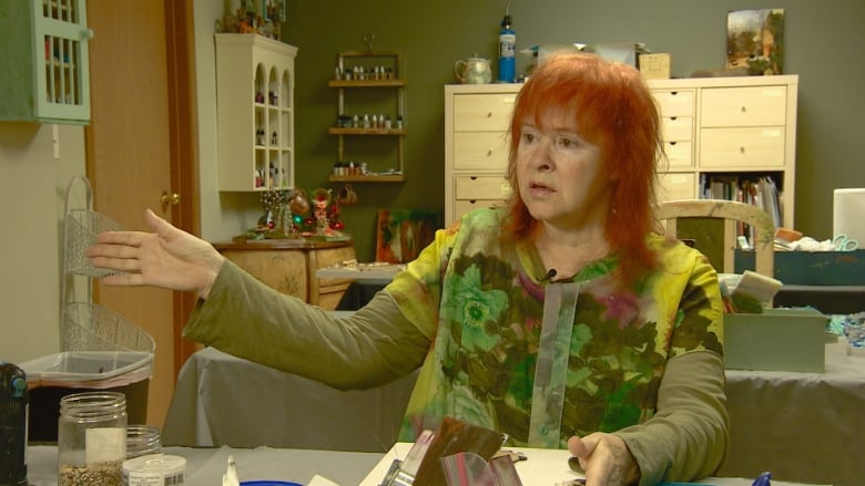 Woman dressed in green in a cluttered green art room speaks animatedly.