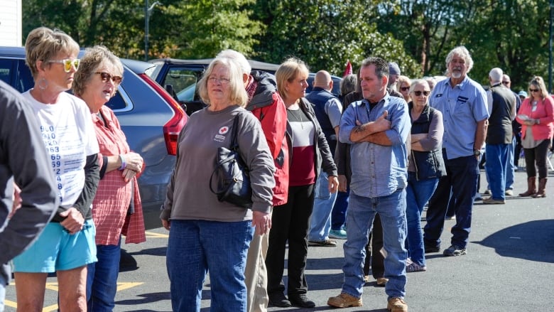 About 20 people, predominantly older men and women, are shown lining up outdoors.