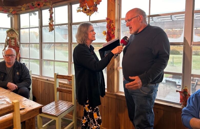 Woman holds a microphone to a man's face in a restaurant. 