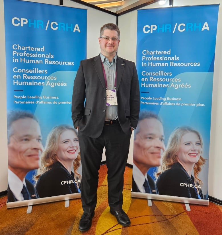 A man in a suit stands in front of two vertical signs that read CPHR/CRHA Chartered Professionals in Human Resources.