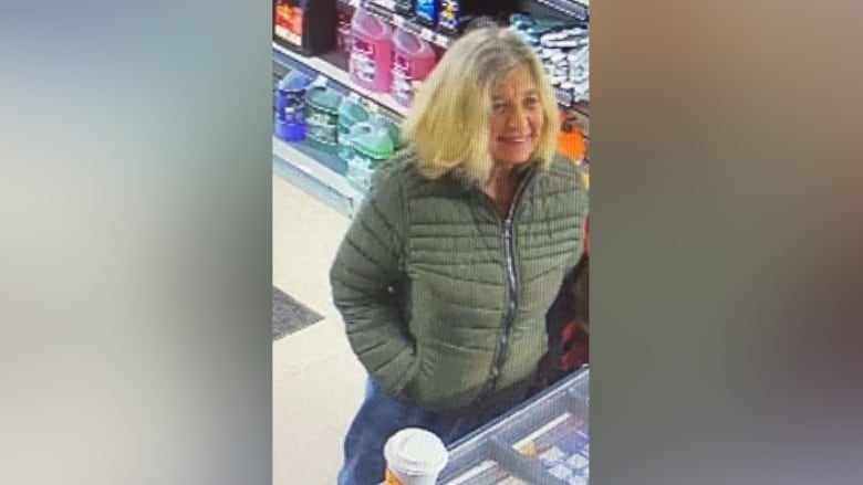 A woman with shoulder-length blonde hair and a green jacket smiles at a counter.