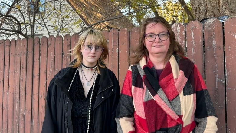 A mother and son stand outside in front of a fence.