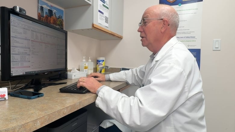 Doctor Bob Irvine is sitting at a computer in a white coat in his office.