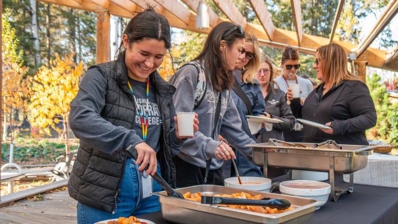 People are seen serving themselves food at tables set up outside.