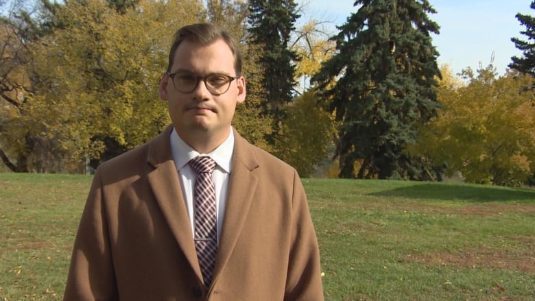 A man in a brown suit poses for a photo.