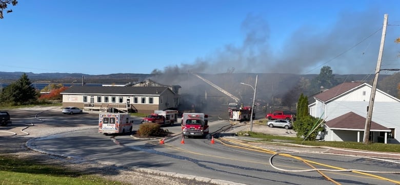 A view from a street looking at a building. Behind it there is smoke and fire trucks parked around it.