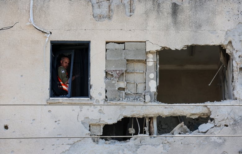 A first responder is seen in the window of a heavily damaged building.