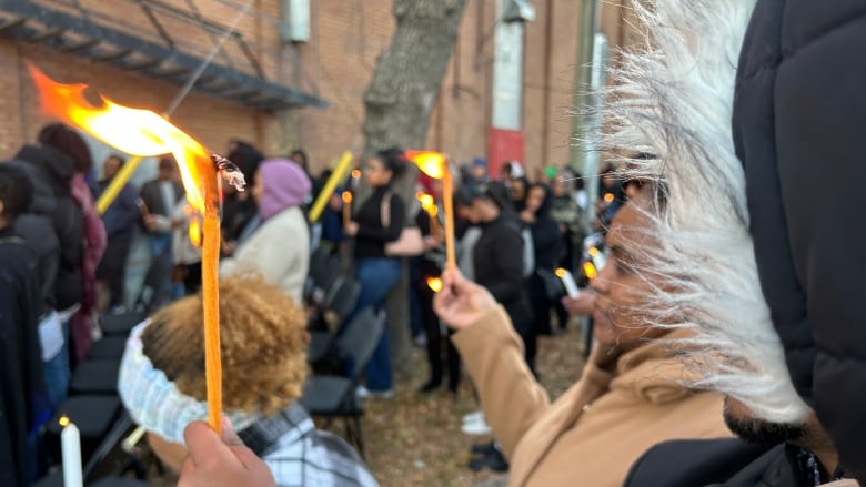 People holding up candles outside a building.