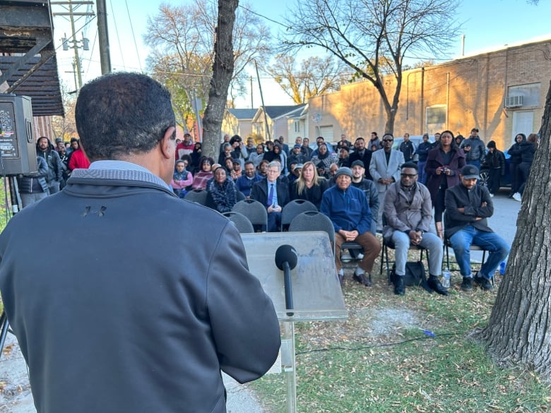 A photo of a man speaking to people from behind a podium.