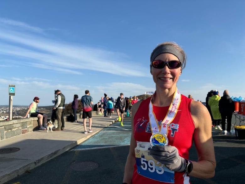 A woman holding a medal and wearing a red tank top. She is wearing sunglasses and smiling. 