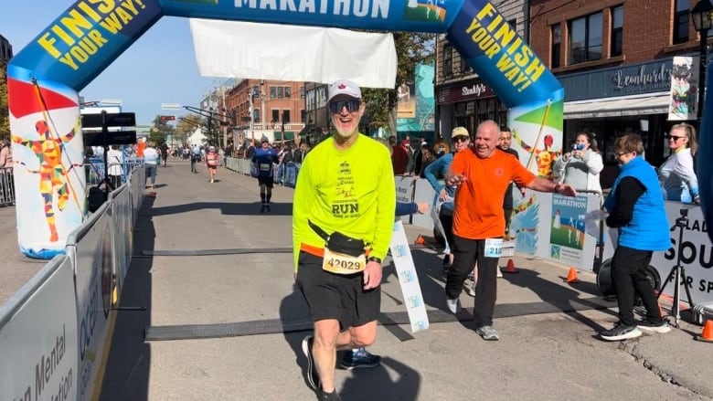 Man in yellow shirt crossing finish line of marathon.