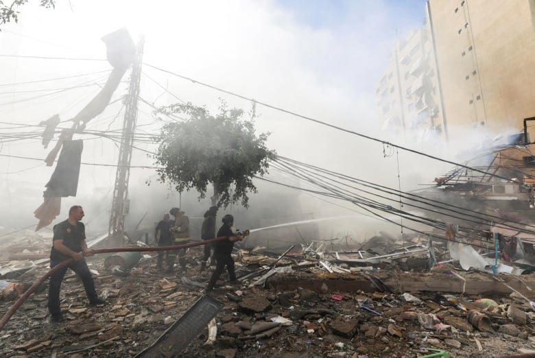 Firefighters put use a hose amid smoke and the rubble of a destroyed building.