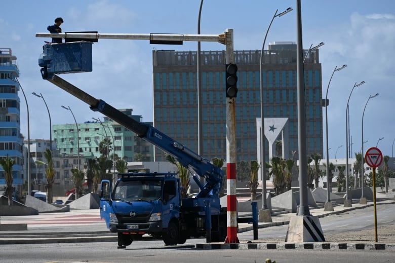 A person stands on the raised platform of a utility truck as they work on fixing a street light.