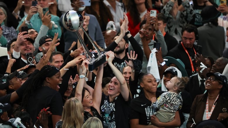 Women celebrate a basketball championship with the trophy.