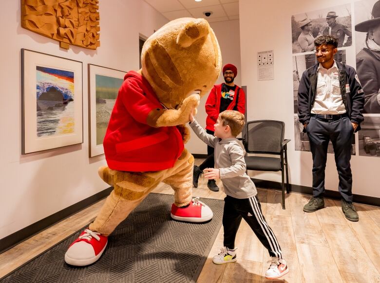 a costumed mascot high fives with a young boy as two poeple behind laugh