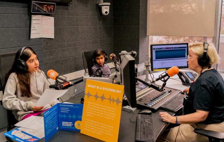 A woman in a radio studio interviews two young children 