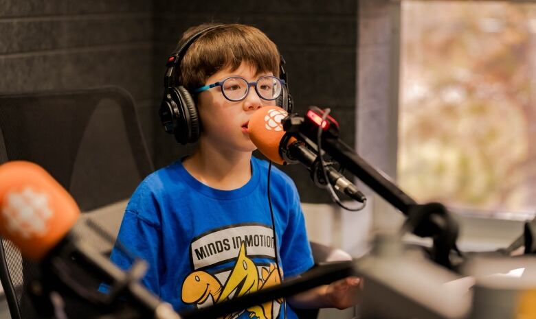 a young boy in a blue shirt speaks into an orange microphone