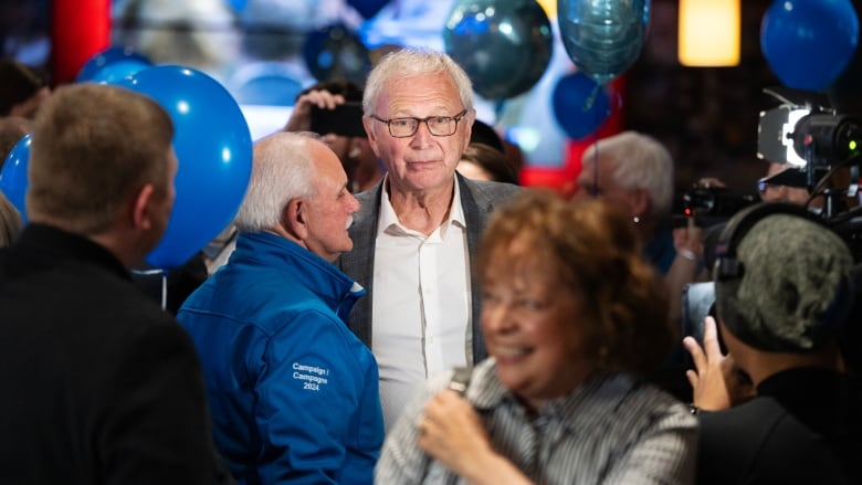 A man stands quietly in the middle of a raucous crowd, looking sad.