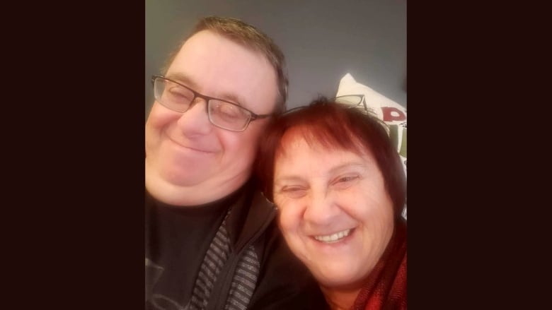 A man with glasses and short brown hair and a woman with reddish hair put their heads together and smile.