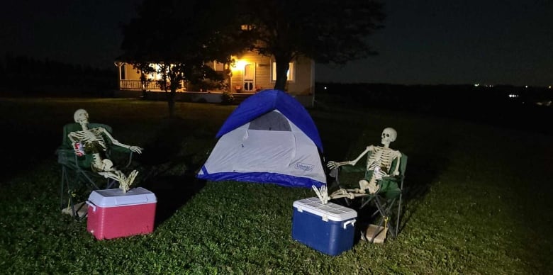 Skeletons sitting by a camping tent.