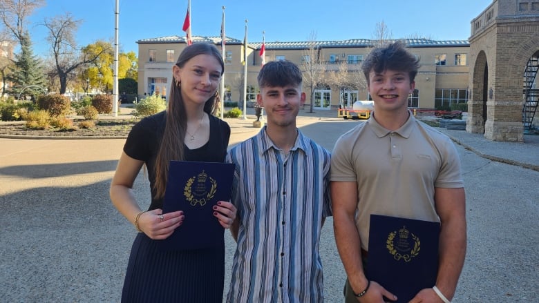 Three teens stand holding certificates.