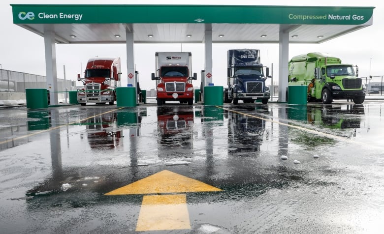 four semi tractor trailers are seen side by side at a filling station from a distance head on