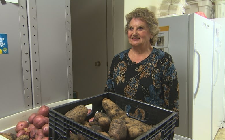 A woman stands smiling next to a bin of dirty potatoes, fresh from the garden,