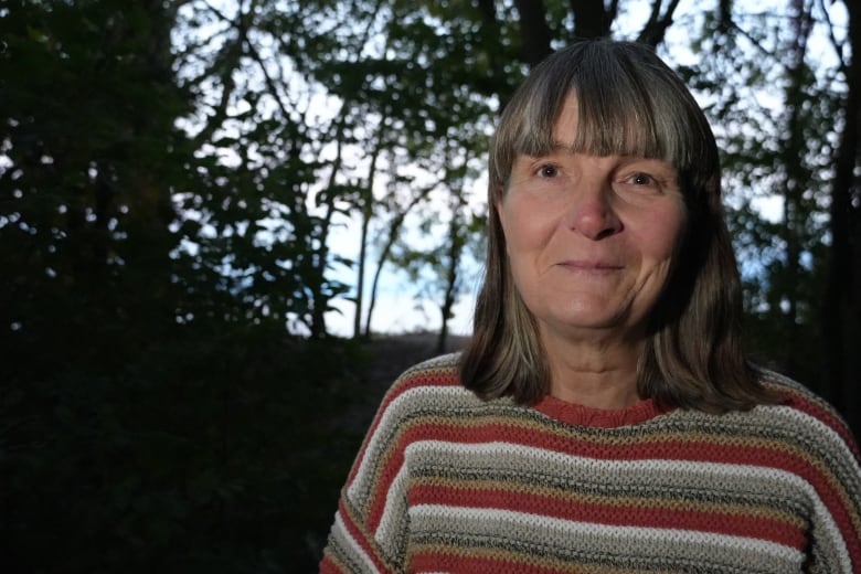 A woman stands with trees behind her in the dwindling light.