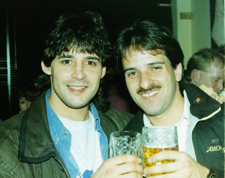 Two men smile holding beers. 