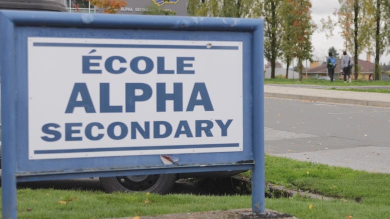 A blue sign on green grass says cole Alpha Secondary