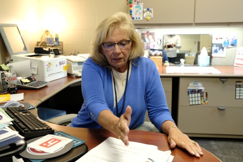 A woman gestures to a stack of papers on her desk.