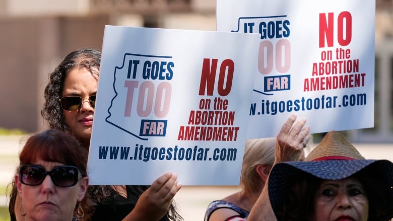 People hold up signs with the slogan 'it goes too far' printed in red and blue ink.