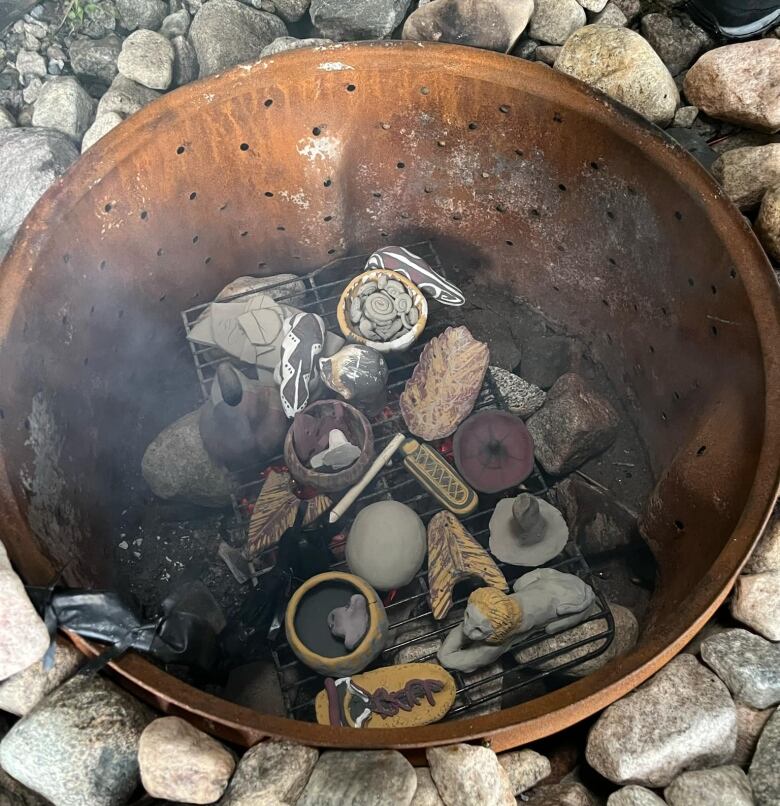 A makeshift kiln using a large metal bowl in a fire pit to harden clay. 