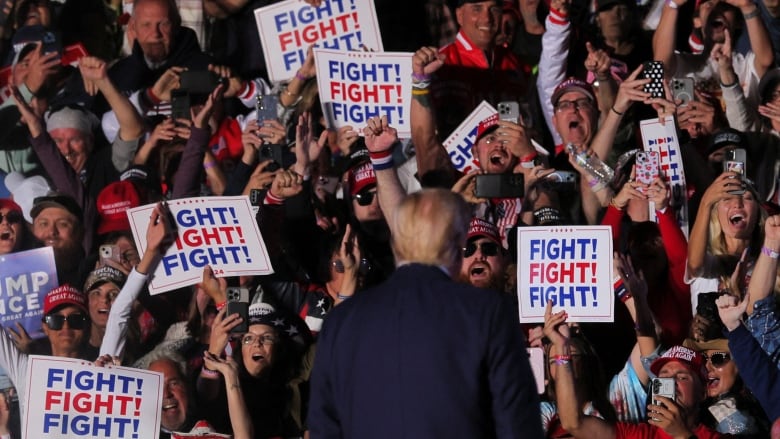 Trump on stage, surrounded by signs that say, 